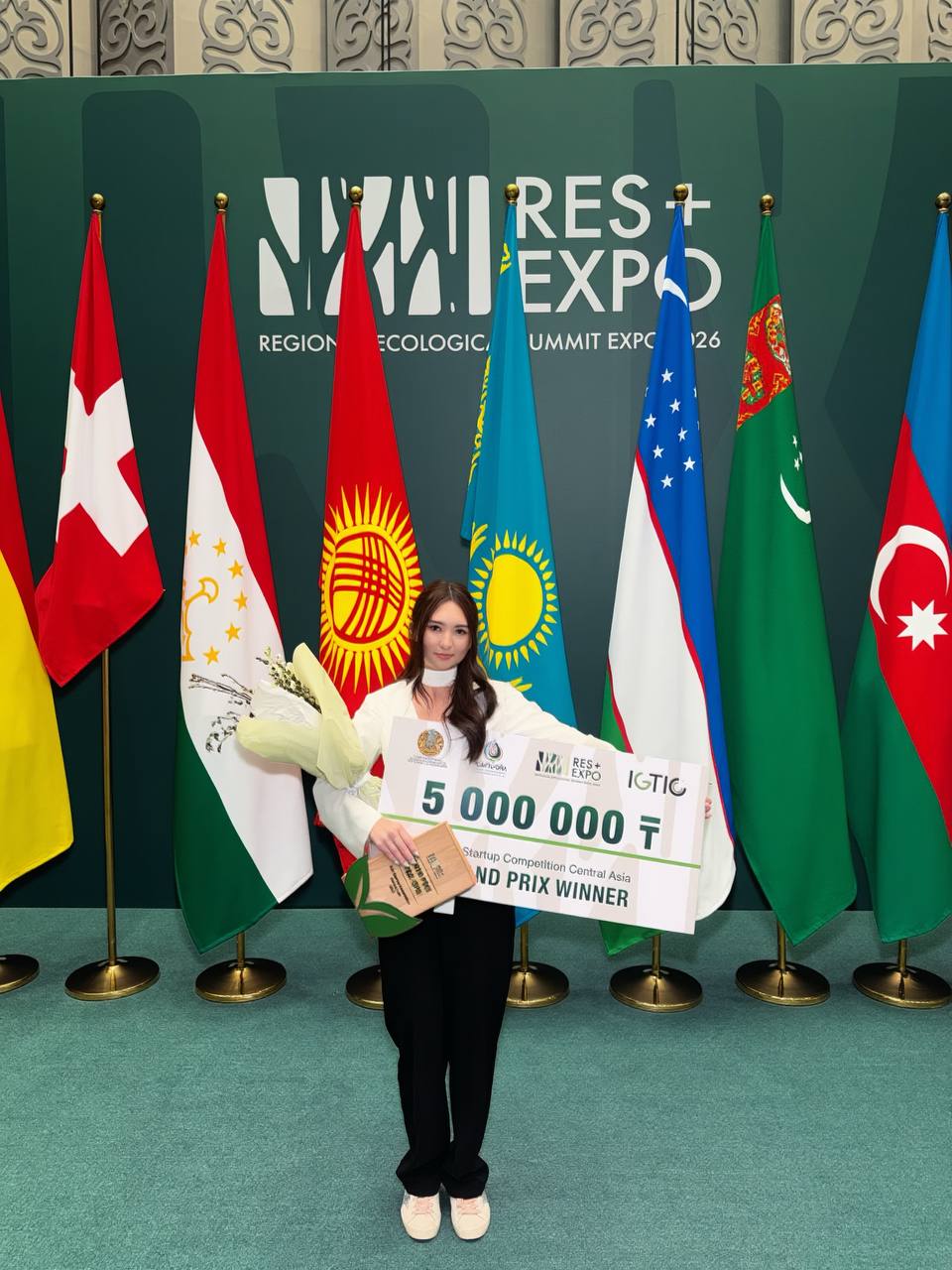 Narmina holding the 5,000,000 ₸ Grand Prix check at RES+EXPO in front of international flags